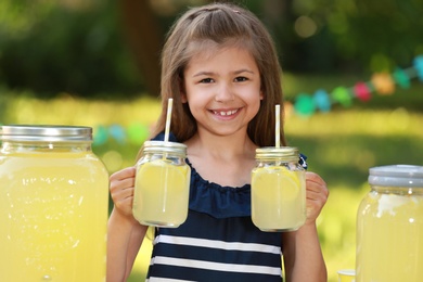 Cute little girl with natural lemonade in park. Summer refreshing drink