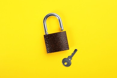 Modern padlock with key on yellow background, flat lay