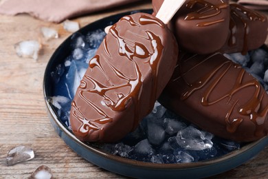 Delicious glazed ice cream bars and ice cubes on wooden table, closeup