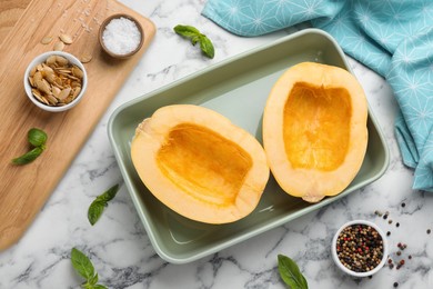 Photo of Raw spaghetti squash halves in baking dish with basil and spices on white marble table, flat lay