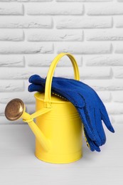 Photo of Yellow watering can with gardening gloves on white wooden table