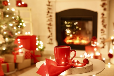 Red cup and festive lights on white table in room with Christmas decorations. Interior design