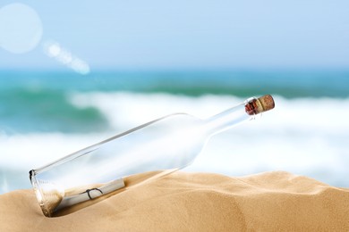 Corked glass bottle with rolled paper note on sandy beach near ocean