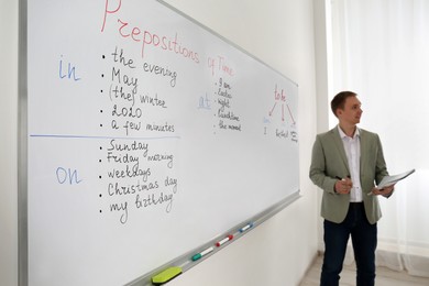 English teacher giving lesson on prepositions of time near whiteboard in classroom