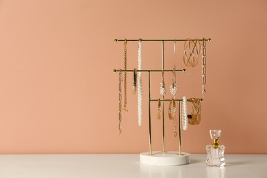 Holder with set of luxurious jewelry and perfume on white table near pale pink wall, space for text