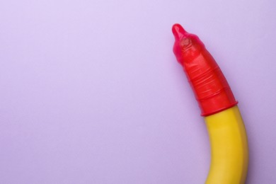 Banana with condom on lilac background, top view and space for text. Safe sex concept