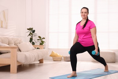 Overweight woman doing exercise with dumbbells at home, space for text