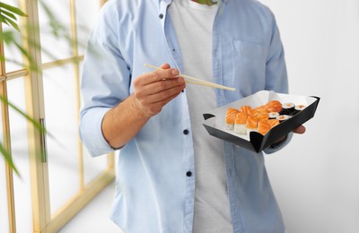 Photo of Man eating sushi rolls with chopsticks indoors, closeup