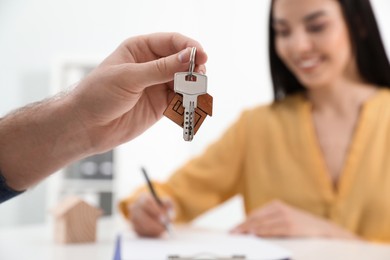Happy young woman signing purchase contract in office. Real estate agent holding new house key, closeup