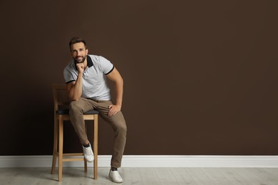 Handsome man sitting on stool near brown wall. Space for text