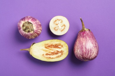 Photo of Cut and whole raw ripe eggplants on violet background, flat lay