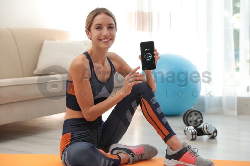 Photo of Young woman showing smartphone with fitness app at home