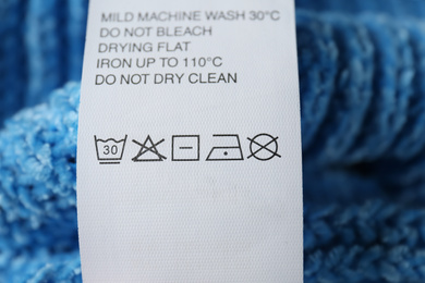 Clothing label with care symbols on blue sweater, closeup view