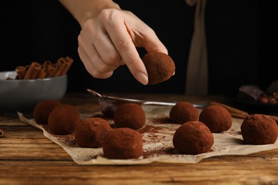 Photo of Woman preparing delicious chocolate truffles at wooden table, closeup
