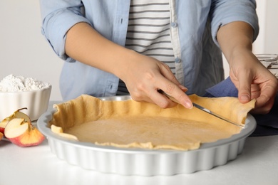 Woman cutting dough leftovers for traditional English apple pie in baking dish at white table, closeup