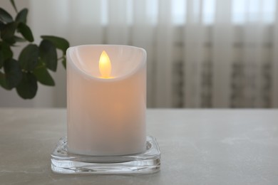 Glowing decorative LED candle on grey table. Space for text