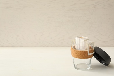 Drip coffee bag in glass cup on white table. Space for text