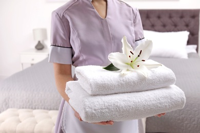 Maid holding fresh towels with flower in hotel room, closeup