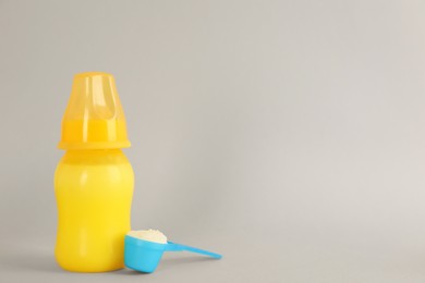 Feeding bottle with infant formula and scoop of powder on light grey background, space for text. Baby milk