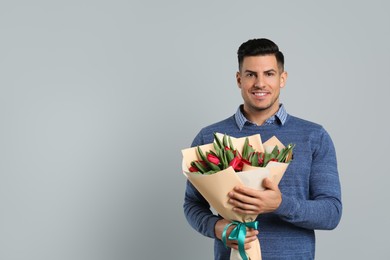 Photo of Happy man with red tulip flowers bouquet on light grey background, space for text. 8th of March celebration