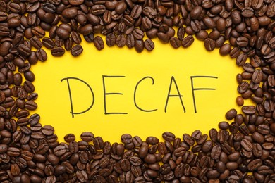 Word Decaf and coffee beans on yellow background, flat lay