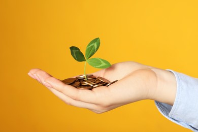 Woman holding coins with green sprout on yellow background, closeup. Investment concept