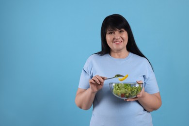 Beautiful overweight woman eating salad on light blue background, space for text. Healthy diet
