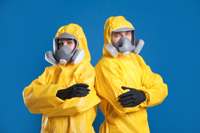 Man and woman wearing chemical protective suits on blue background. Virus research