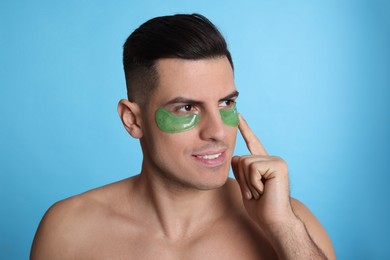 Man applying green under eye patch on light blue background