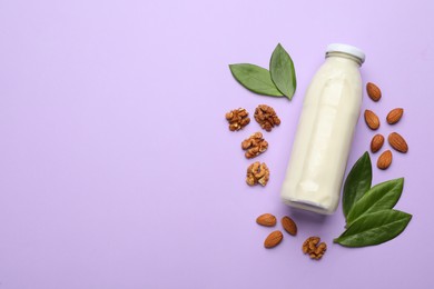 Bottle of vegan milk, walnuts and almonds on violet background, flat lay. Space for text