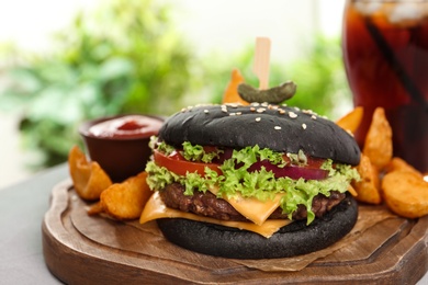 Photo of Juicy black burger and french fries on wooden board, closeup