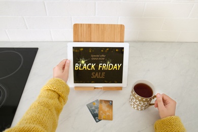 Woman using tablet with Black Friday announcement at kitchen counter, closeup