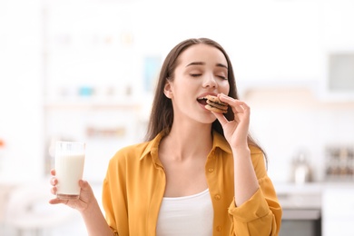 Photo of Beautiful young woman drinking milk with cookies at home