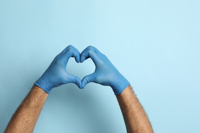 Doctor in medical gloves making heart with hands on light blue background, closeup. Space for text