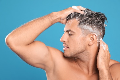 Handsome man washing hair on light blue background