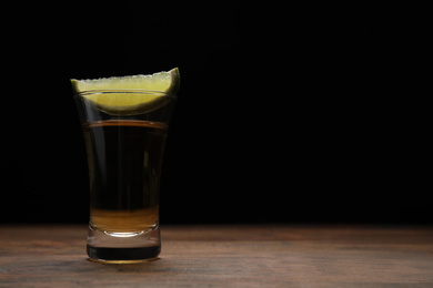 Mexican Tequila shot with lime slice on wooden table against black background. Space for text