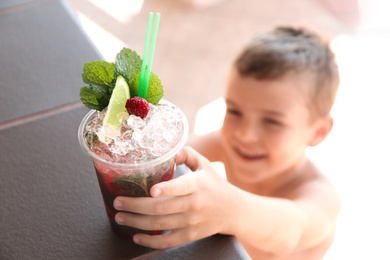 Boy with delicious refreshing drink outdoors, focus on plastic cup