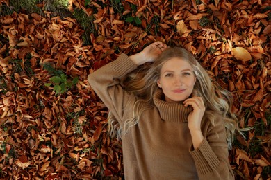 Photo of Portrait of beautiful young woman lying in autumn leaves, top view