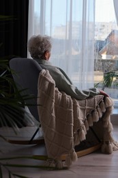 Elderly woman sitting in rocking chair indoors, back view. Loneliness concept