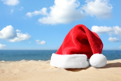 Santa's hat on sandy beach, space for text. Christmas vacation