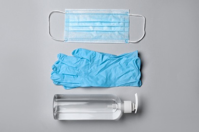 Medical gloves, mask and hand sanitizer on grey background, flat lay