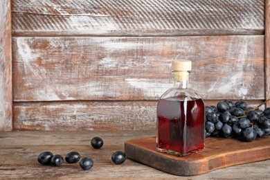 Glass bottle with wine vinegar and fresh grapes on wooden table. Space for text