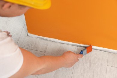 Photo of Worker using brush to paint wall with orange dye indoors, closeup