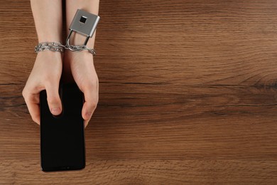 Photo of Woman holding smartphone in chained hands at wooden table, top view. Internet addiction