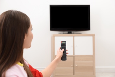 Woman changing TV channel with remote control in living room. Space for text
