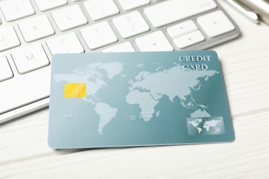 Credit card near computer keyboard on white wooden table, closeup