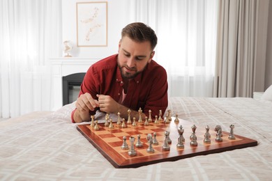 Young man playing chess alone on bed at home