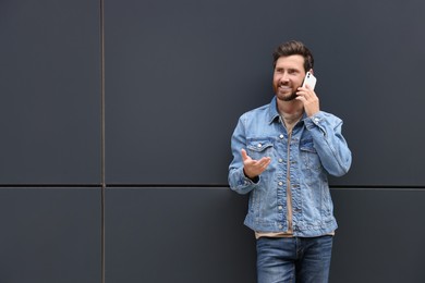 Photo of Handsome bearded man talking on smartphone near grey wall outdoors. Space for text