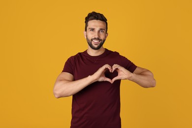 Happy man making heart with hands on yellow background