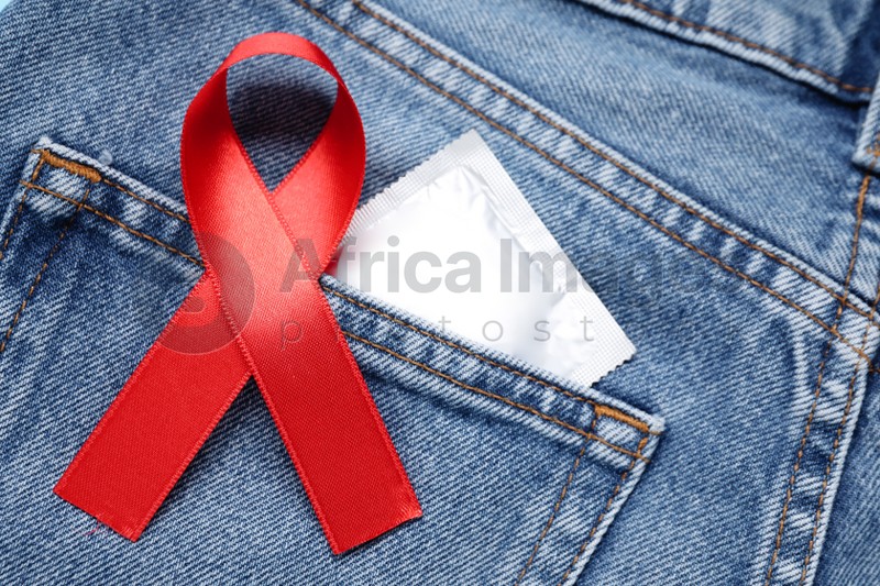 Jeans with red ribbon and condom, closeup. AIDS disease awareness